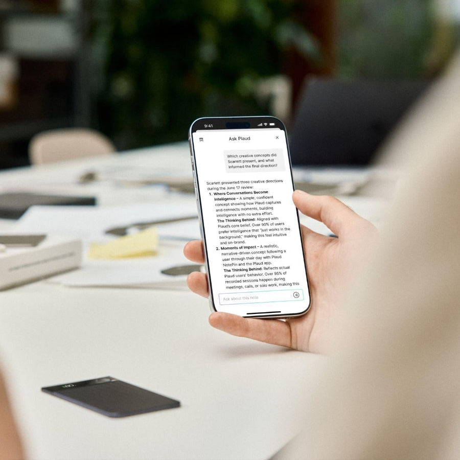 Using the Plaud App on a smartphone with a black Plaud Note AI voice recorder on a white desk.