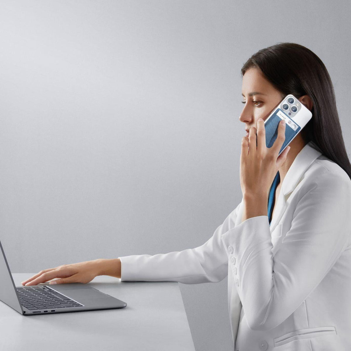 Woman using a blue Plaud Note on her phone to record a call while working at a laptop.