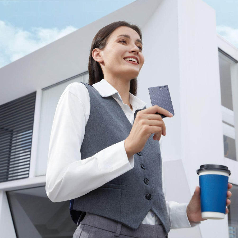 A professional woman holds a starlight Plaud Note and a coffee cup outside a modern office building.