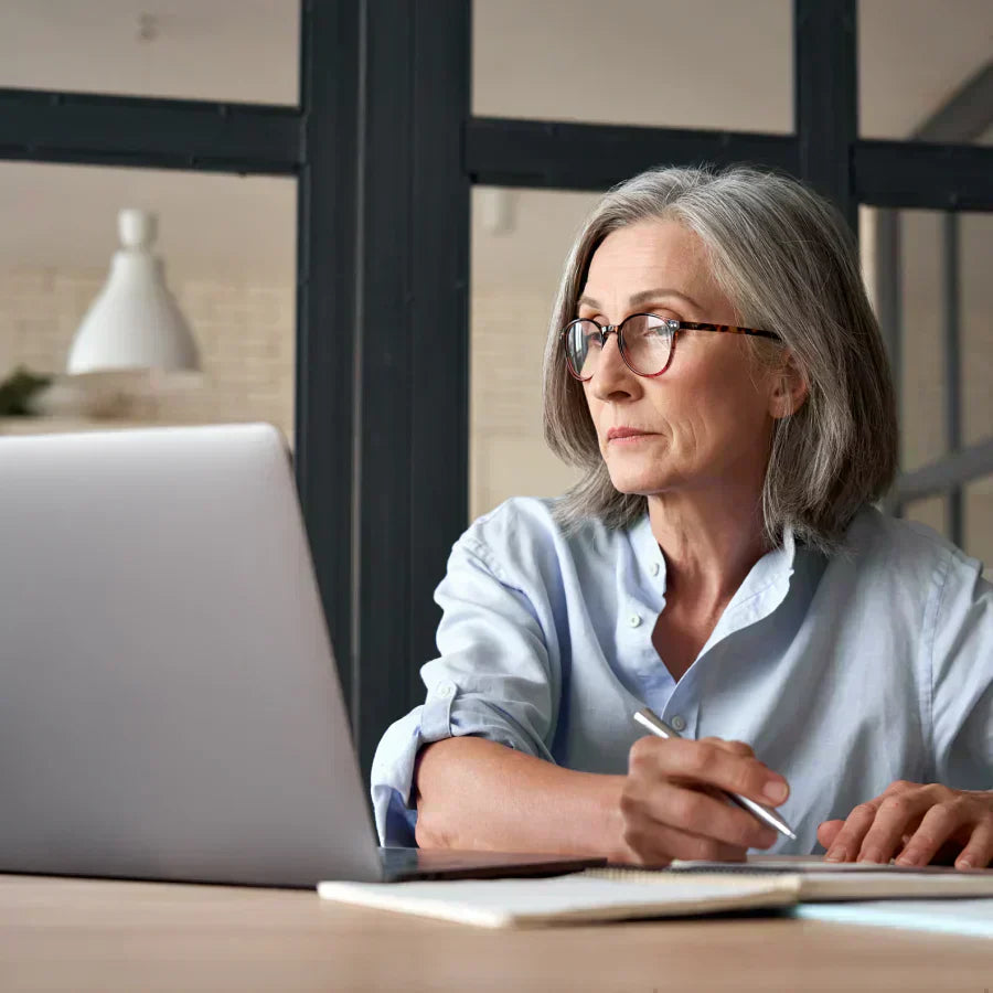 A professional woman wearing a silver Plaud NotePin on her collar while working at a laptop.