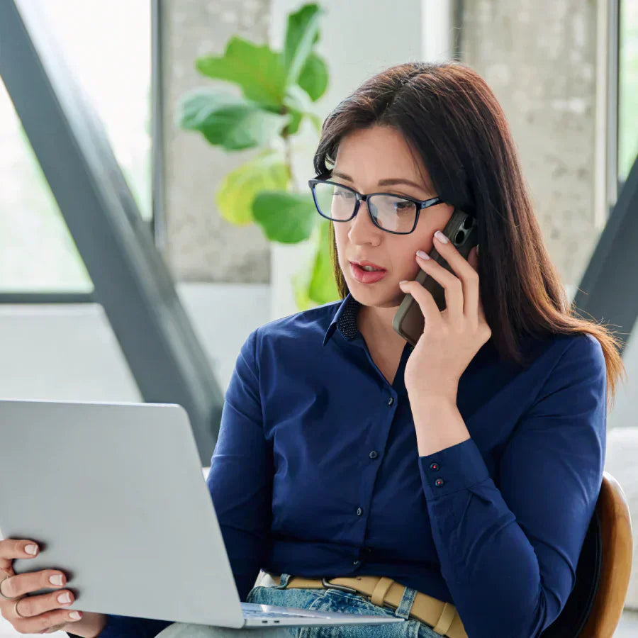 Woman recording a phone call with a black Plaud Note attached to her smartphone while working on a laptop.