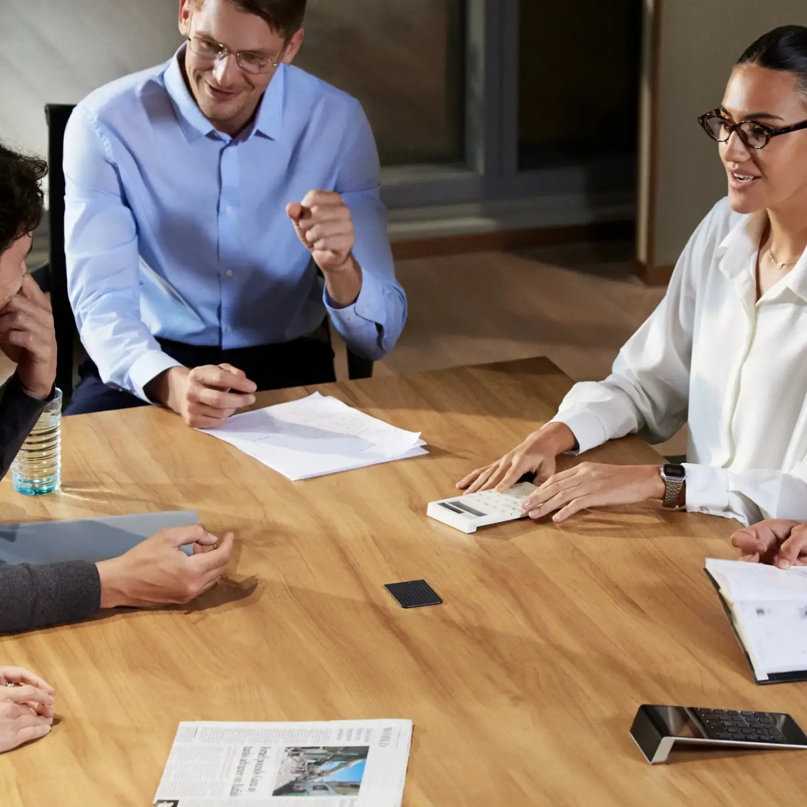 A black Plaud Note on a wooden table during a meeting with professionals, capturing the conversation.
