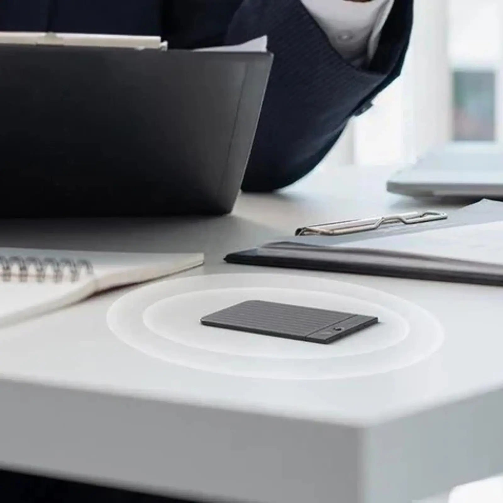 Black Plaud Note on a desk with sound wave graphics, capturing audio during a professional meeting.
