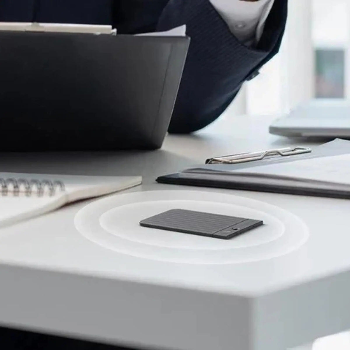 Black Plaud Note on a desk with sound wave graphics, capturing audio during a professional meeting.