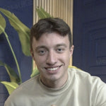 A smiling young man with short brown hair wearing a light-colored sweatshirt.