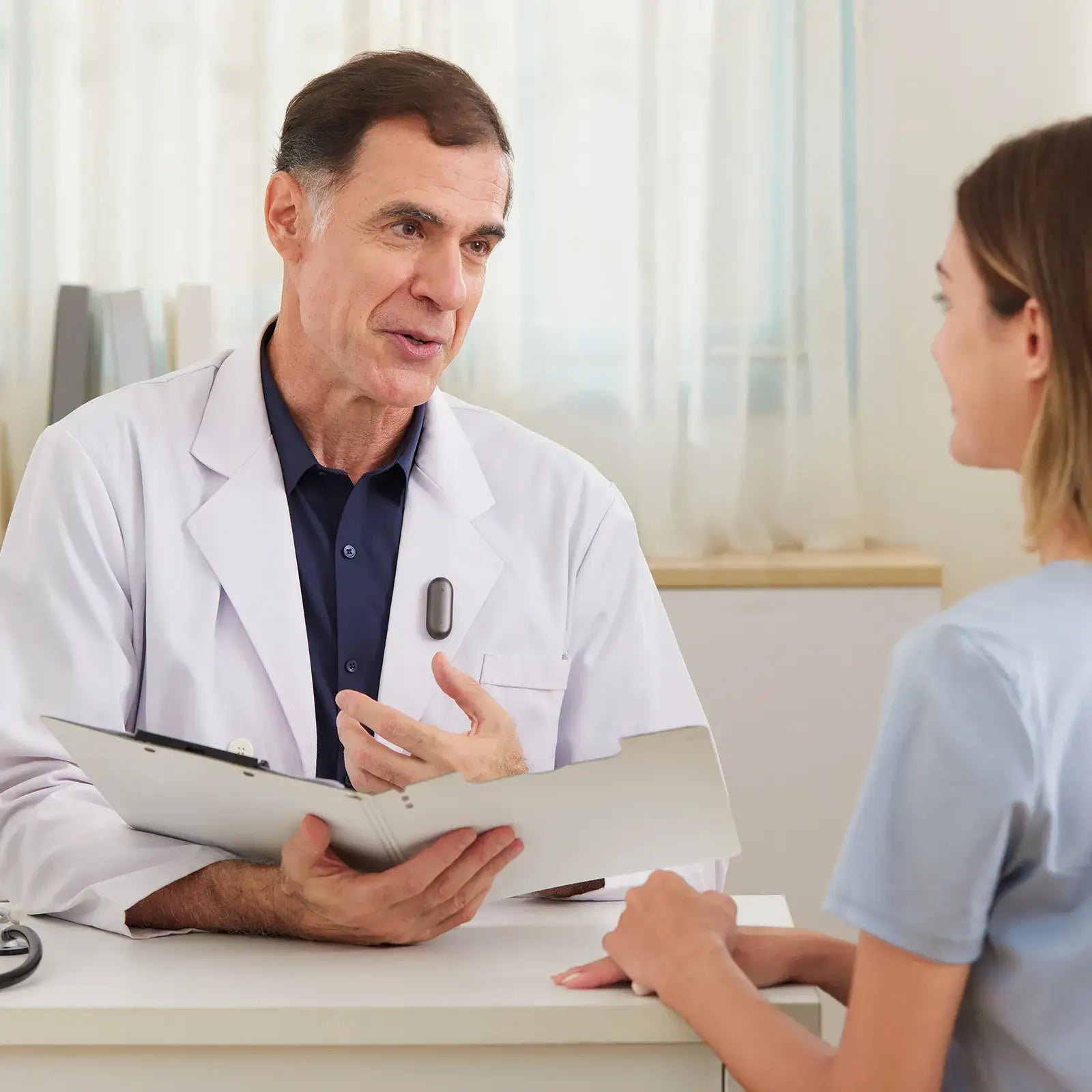 A doctor wearing a black Plaud NotePin on his lapel while consulting with a patient.