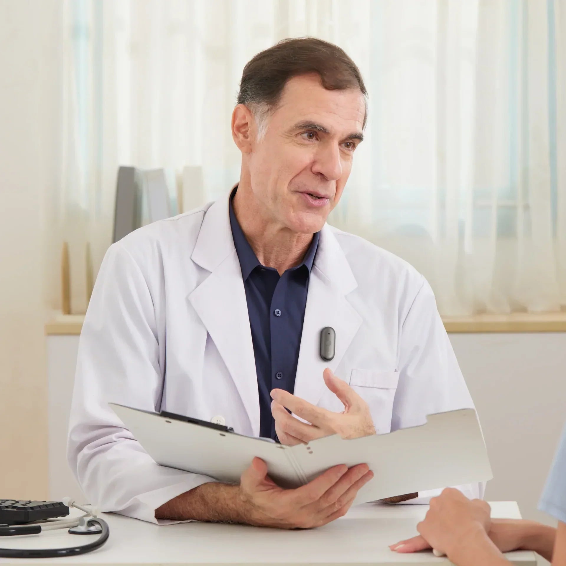 A doctor wearing a Plaud NotePin talks to a patient.