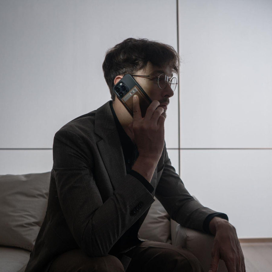 Man in a suit using a gold Plaud Note attached to his phone to record a call.