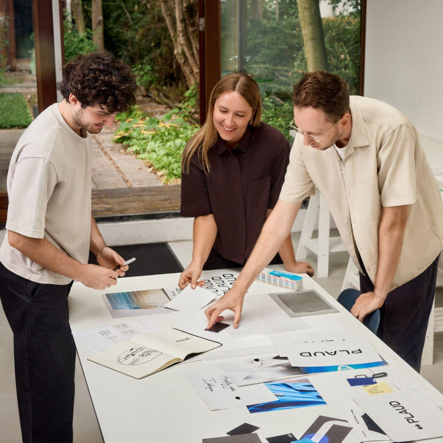Three people in a studio review design materials on a table with a black Plaud Note.