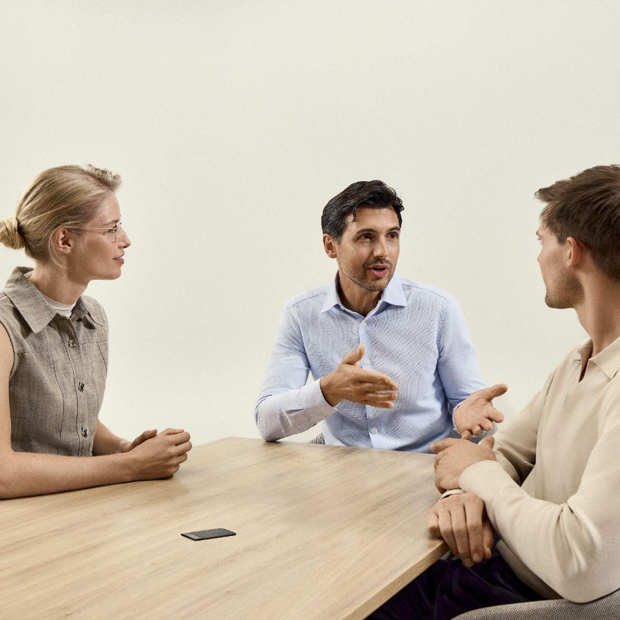 Three professionals converse around a table with a black Plaud Note S capturing the meeting.