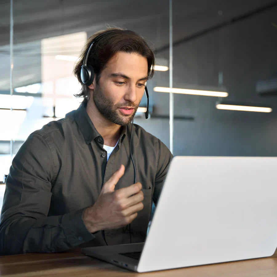 A professional man wearing a headset and using a laptop for a virtual meeting in a modern office.