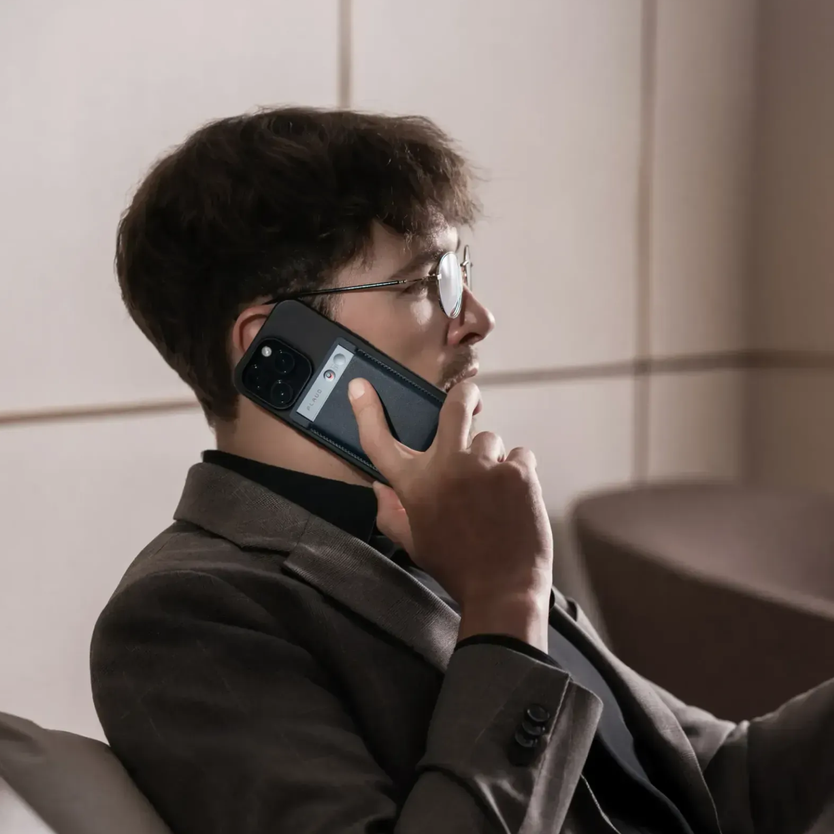 Man using a black Plaud Note attached to his phone to record a call while wearing a suit.