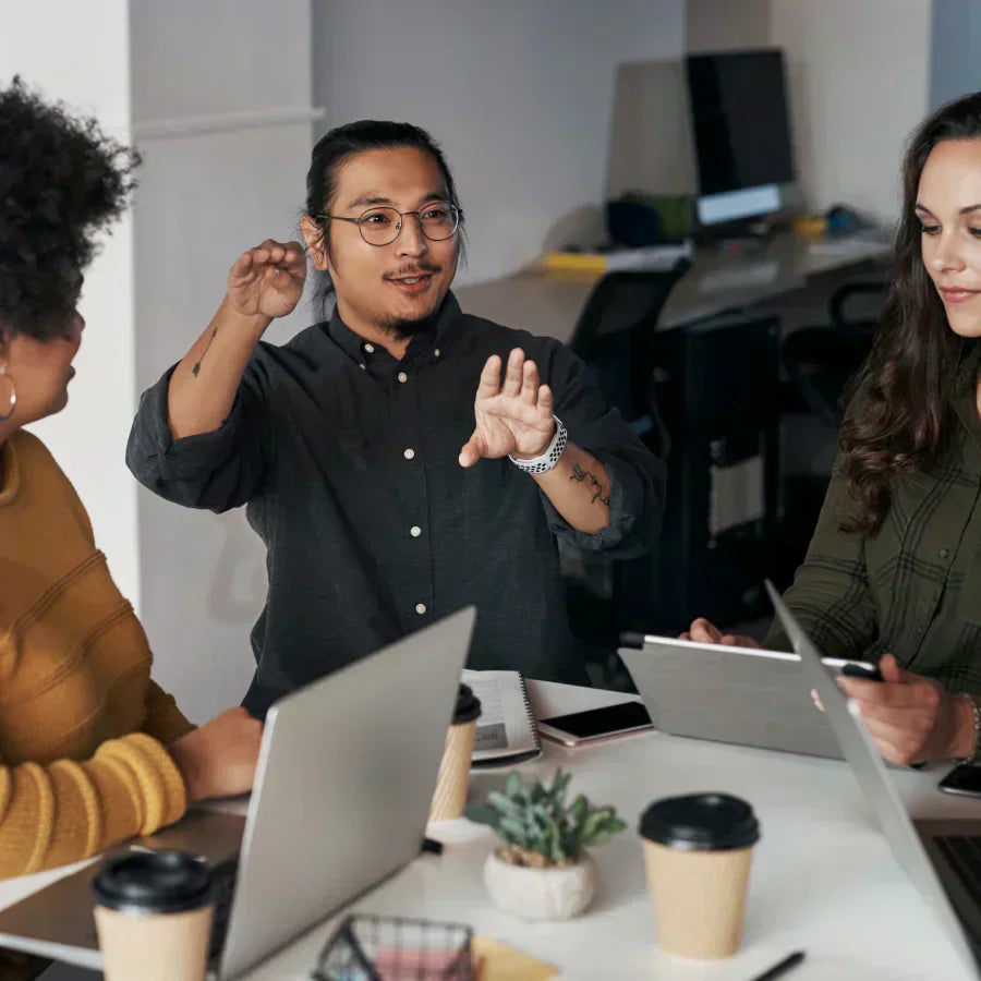Three colleagues collaborating in a meeting with laptops and coffee in a modern office.