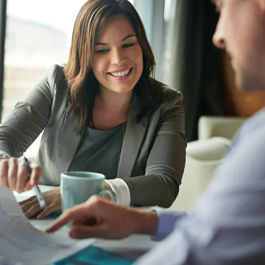 Smiling woman in a blazer reviews documents with a colleague during a professional business meeting.