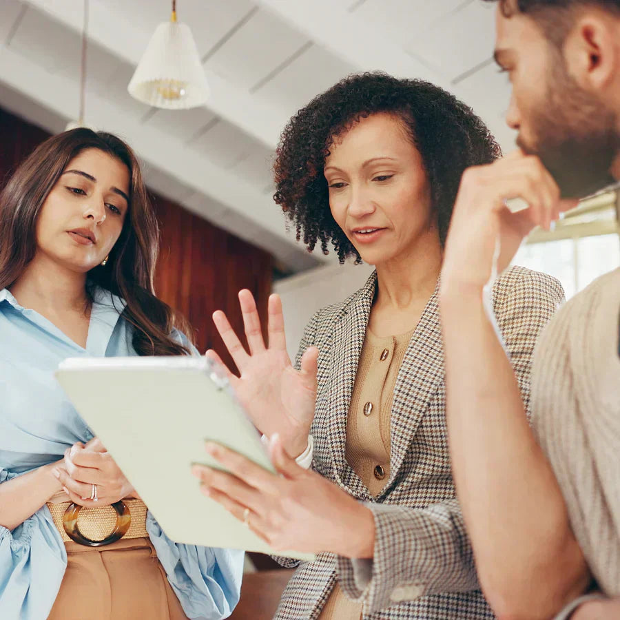 Colleagues discuss a tablet; woman wears a silver Plaud NotePin on her blazer.