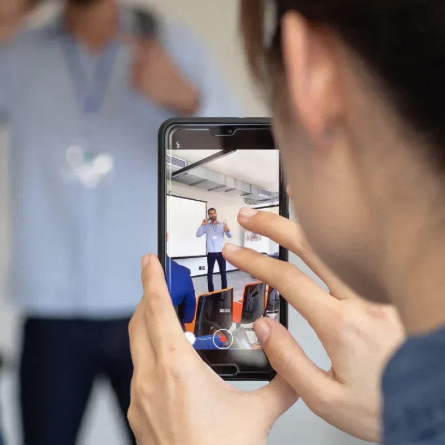 A person records a live presentation on a smartphone, capturing a speaker in a professional setting.