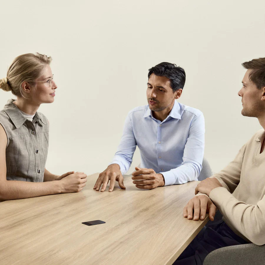 Three people in a meeting with a black Plaud Note Pro on the table recording the discussion.