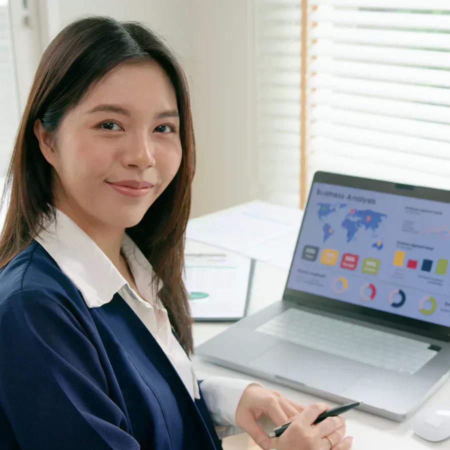 Professional woman in a blue blazer at a desk with a laptop displaying business analysis data.