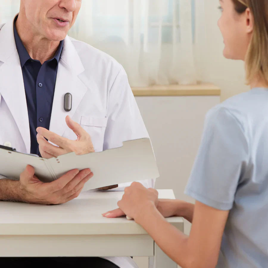 A doctor wearing a Cosmic Gray Plaud NotePin on his white coat while speaking with a patient.