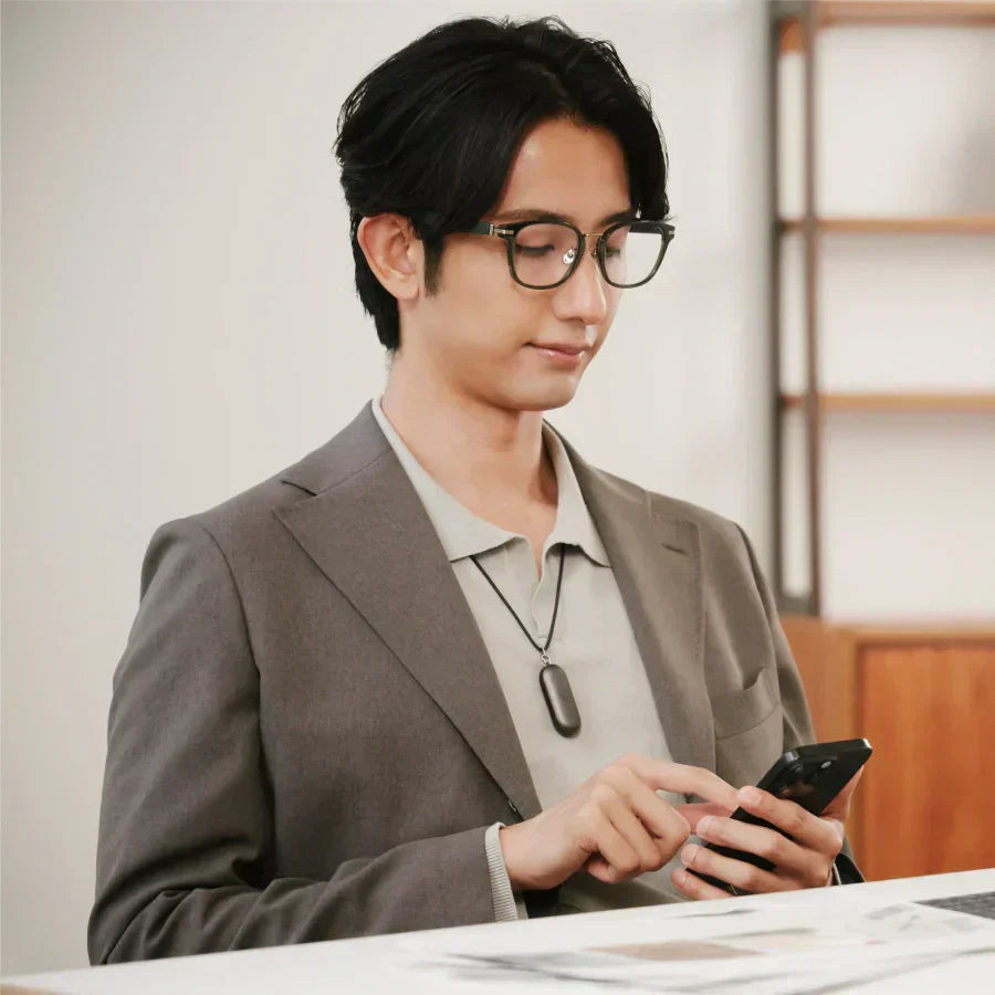Man in a blazer wearing a Cosmic Gray Plaud NotePin S on a lanyard while using a smartphone.