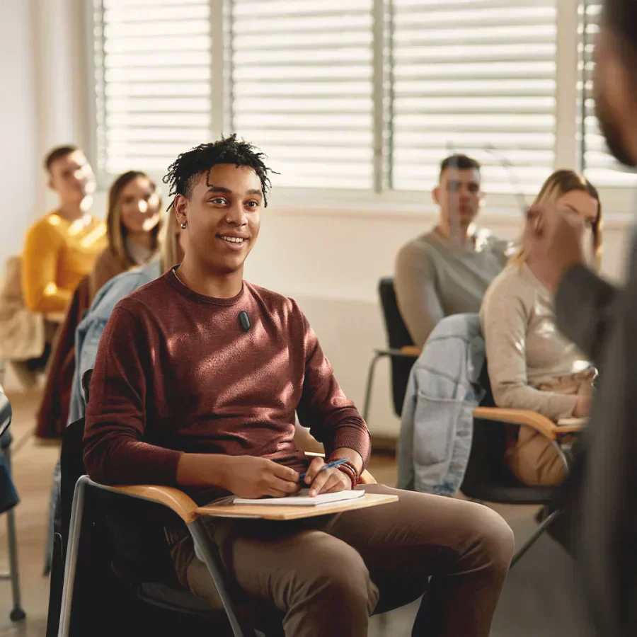 A student wearing a black Plaud NotePin S on his sweater while attending a lecture in a classroom.