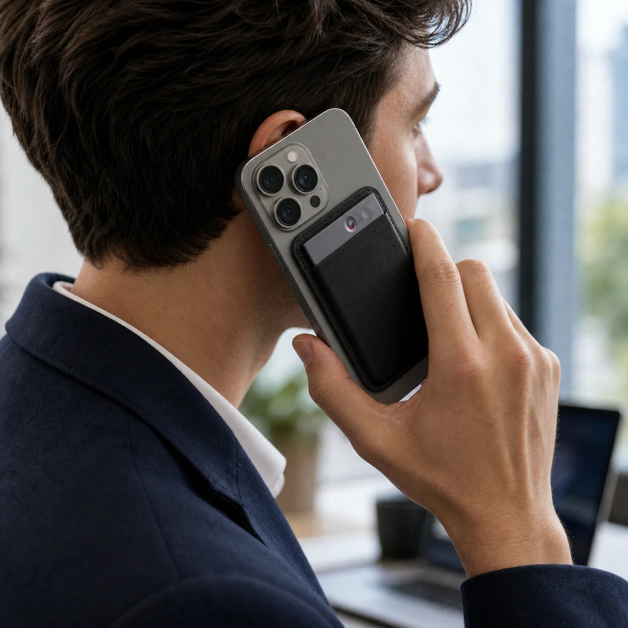 A man in a suit holding a smartphone to his ear with a black wallet attached to the back.