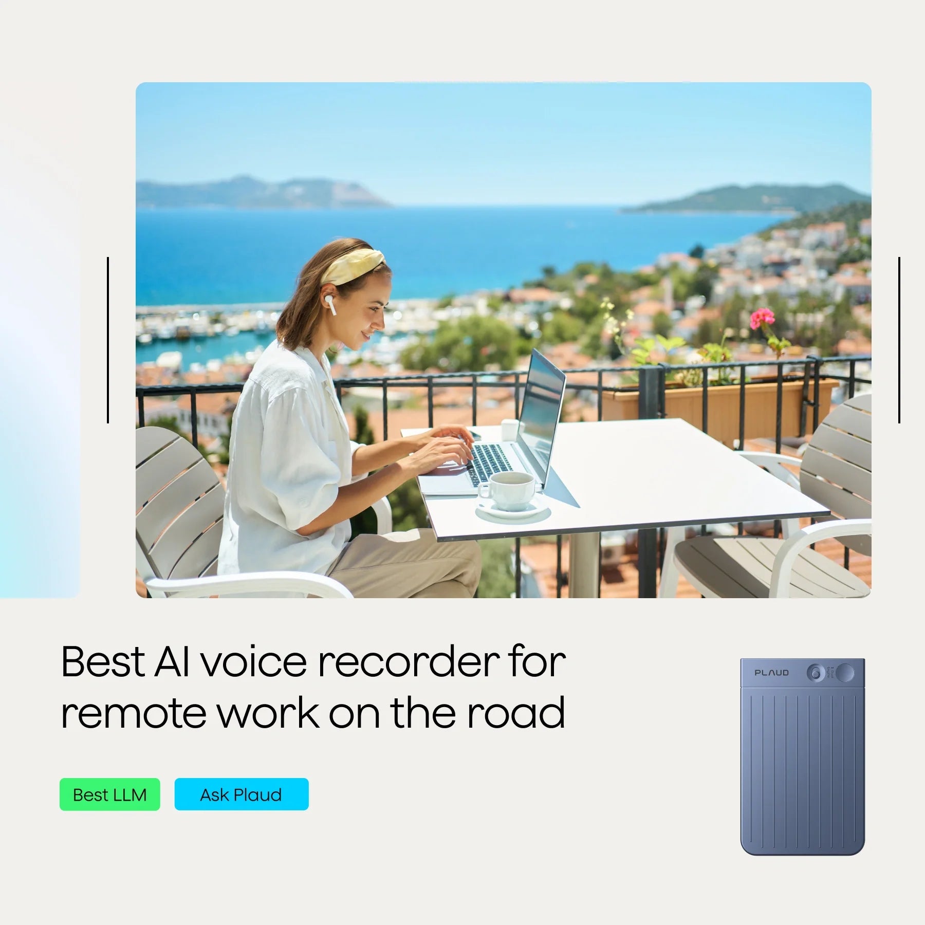 A woman working on a laptop at a table on a balcony with a scenic view of the sea and hills.