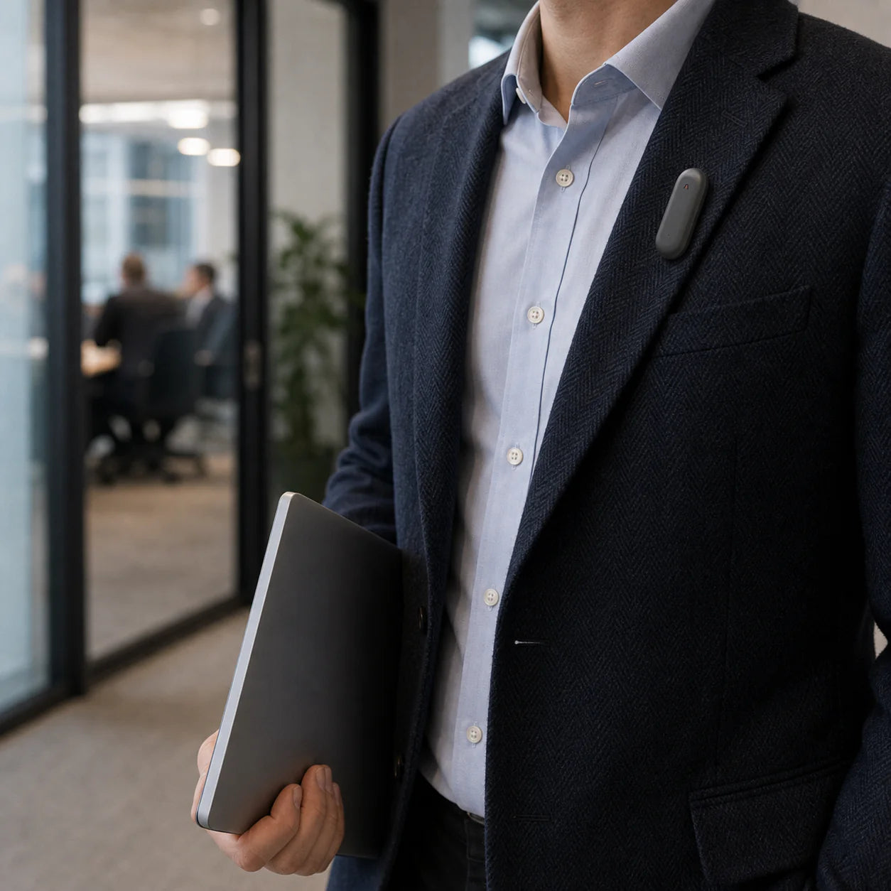A person in a blue blazer holding a laptop with a wearable device attached to the blazer.