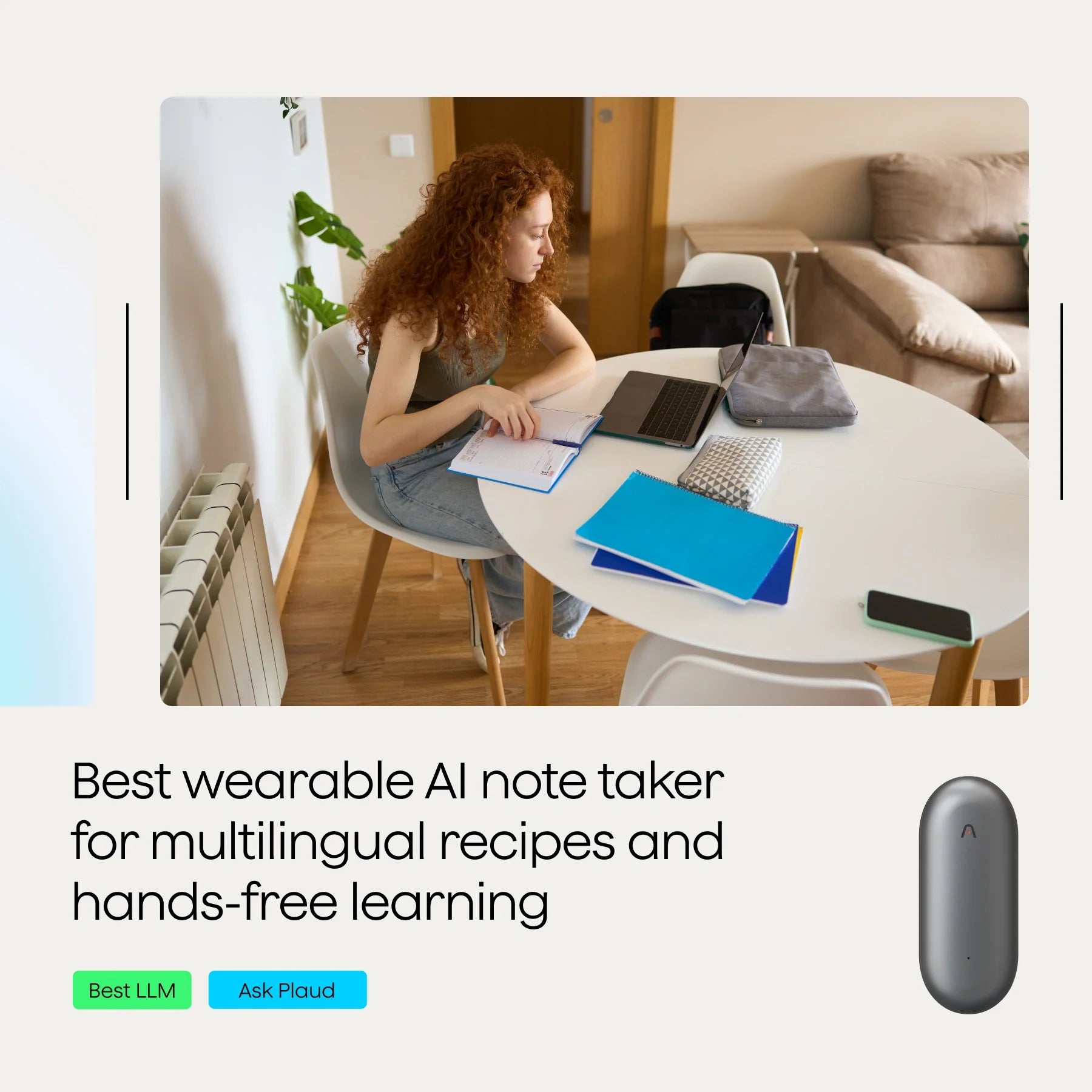 A person with curly red hair sits at a table with a laptop, notebooks, and a smartphone.