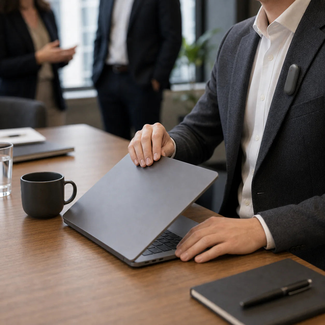 A person in a suit adjusts a laptop on a meeting table, with a coffee cup and notebooks visible.