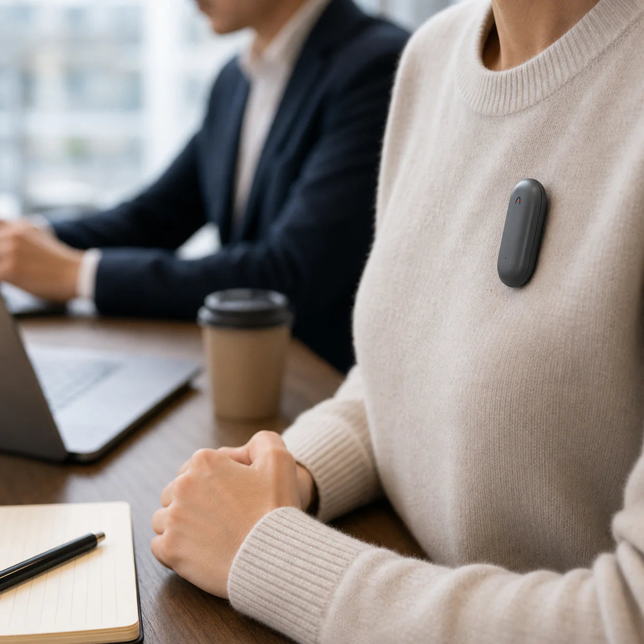 A wearable device attached to a person's sweater, with a notebook and a cup of coffee on the table.