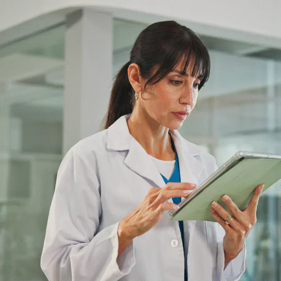 A medical professional in a white lab coat reviews data on a tablet in a clinical setting.