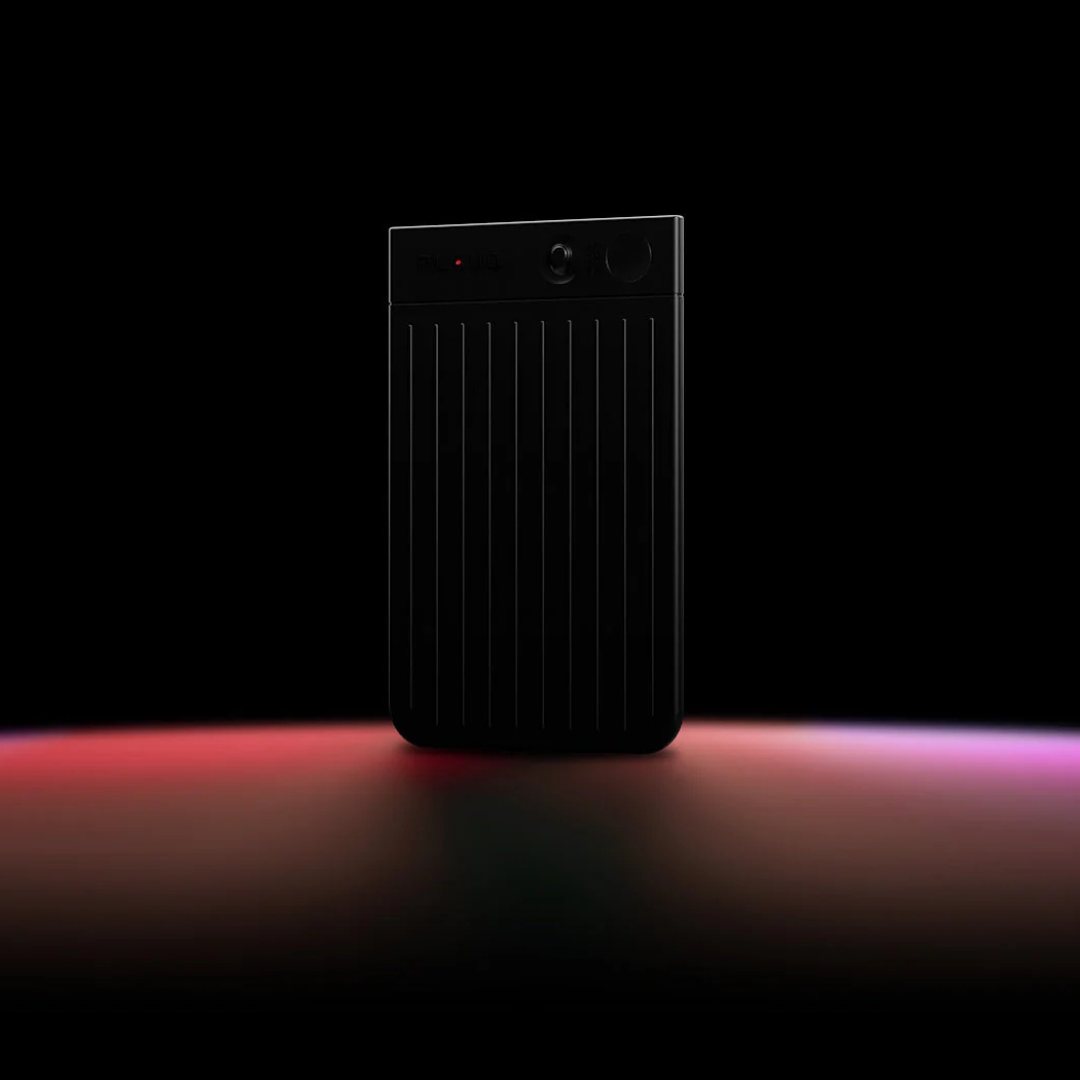 Black Plaud Note AI voice recorder with a ribbed body standing on a surface with red ambient lighting.