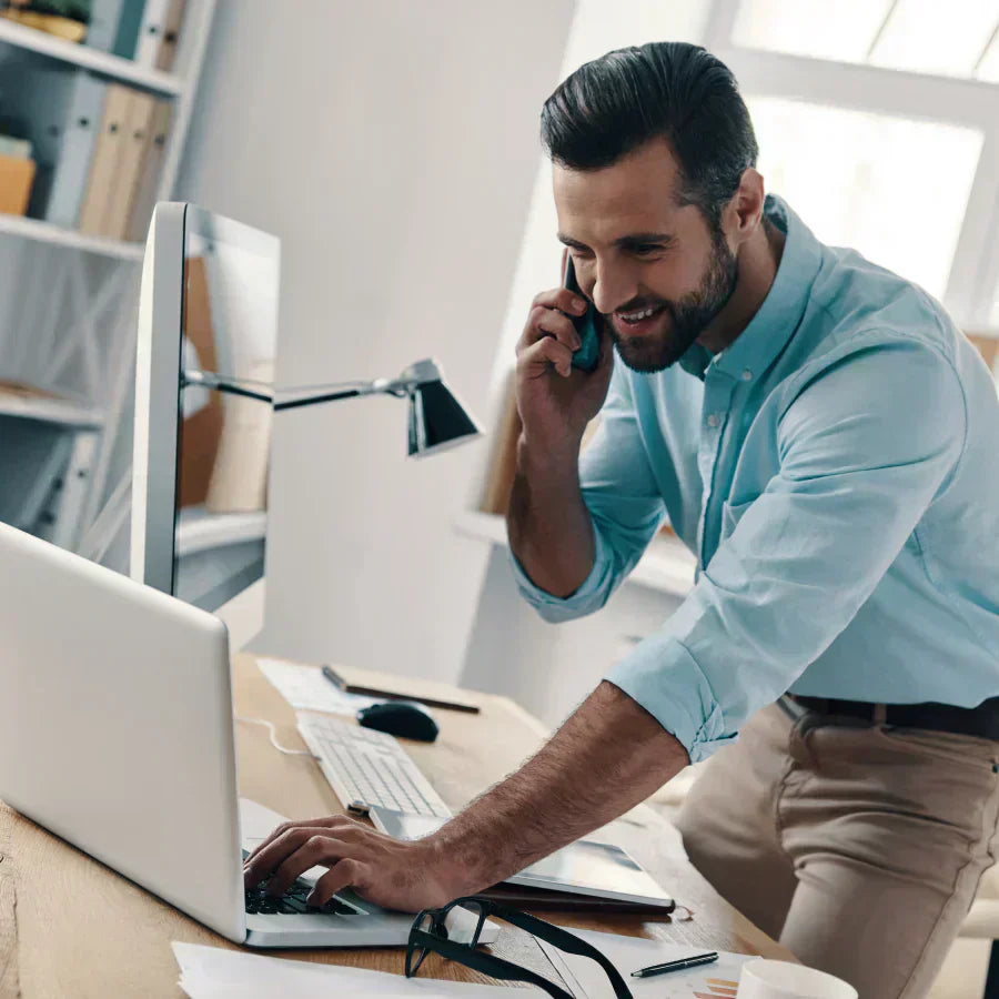 A professional uses a black Plaud Note attached to his phone to record a call while typing on a laptop.