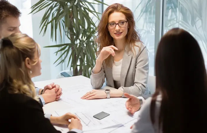 A black Plaud Note records a business meeting as a group of professionals discuss projects around a table.