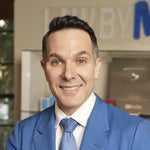 Smiling man wearing a blue suit and patterned tie in a professional office environment.
