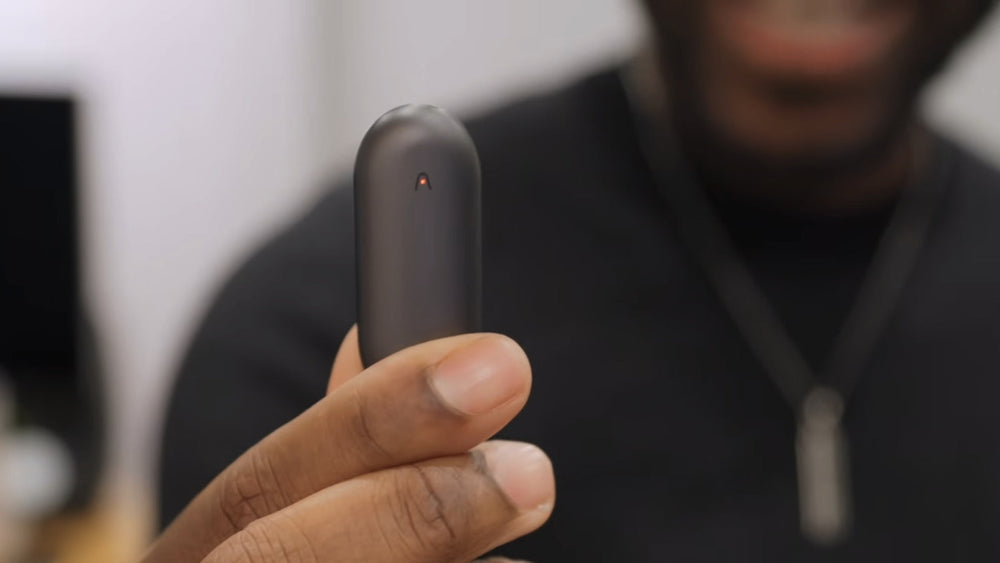 A person holding a Cosmic Gray Plaud NotePin, a small capsule-shaped AI voice recorder.