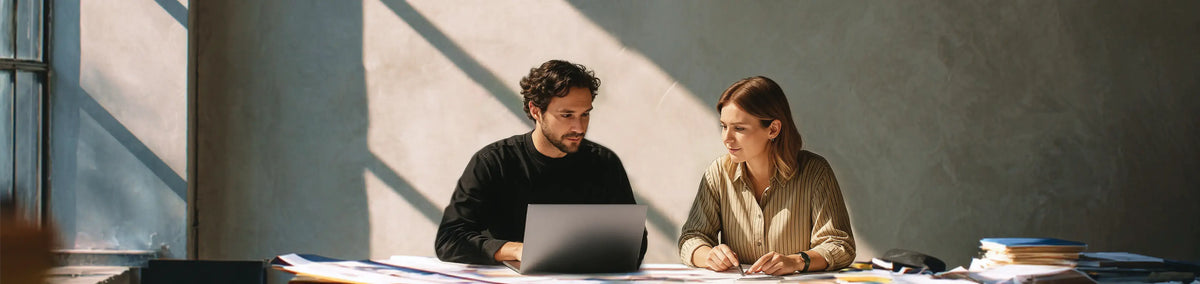 Two professionals collaborating at a desk with a laptop in a sunlit office during a meeting.