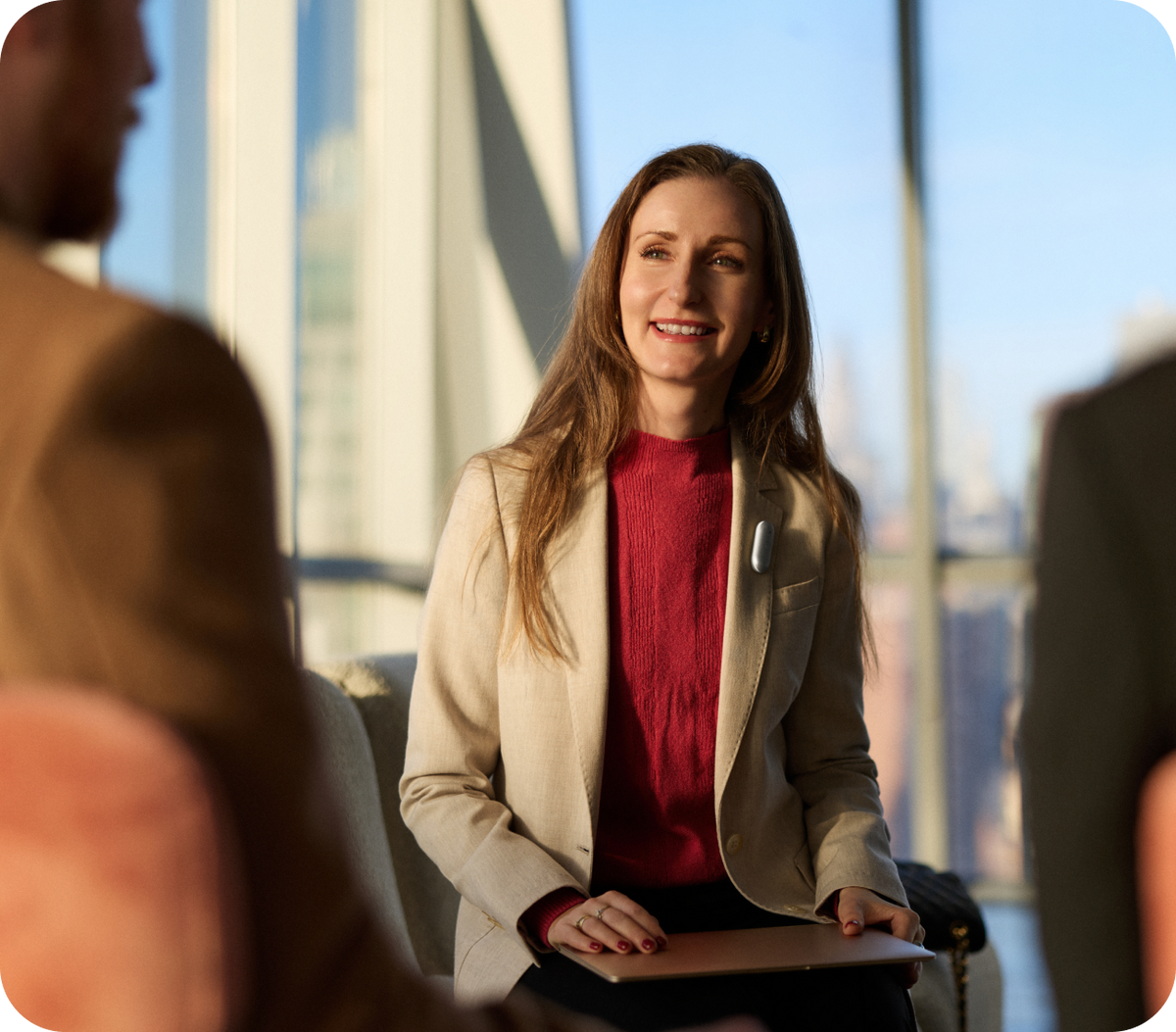 A professional woman smiles during a meeting while wearing a silver Plaud wearable AI recorder on the lapel of her beige blazer.