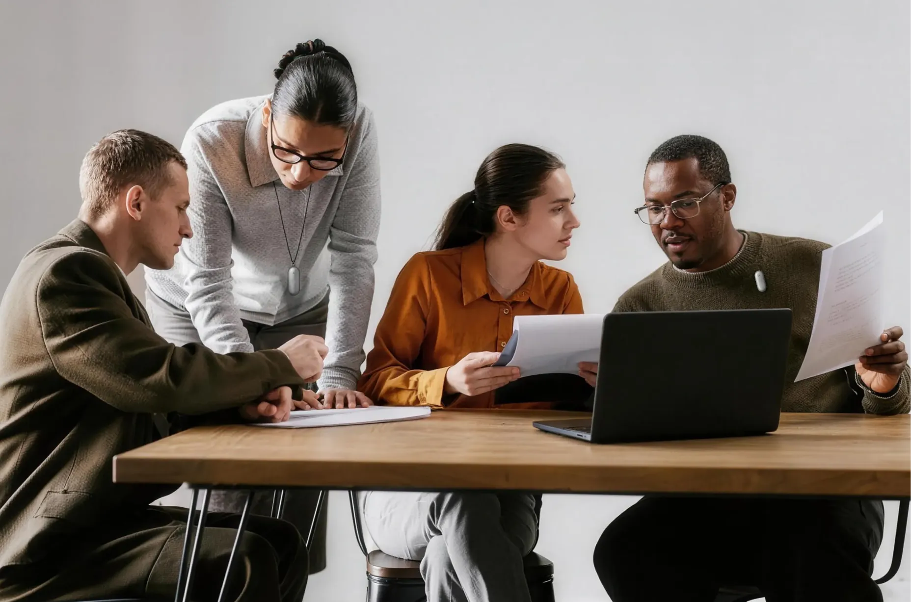 Four professionals collaborate around a laptop and papers, with two people wearing silver Plaud wearable AI recorders.