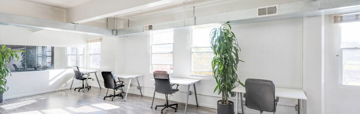 Bright, modern open-plan office with white desks, black chairs, and large windows.