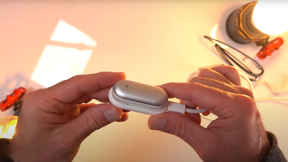 A silver Plaud NotePin being held in hands while connected to a white charging cable.