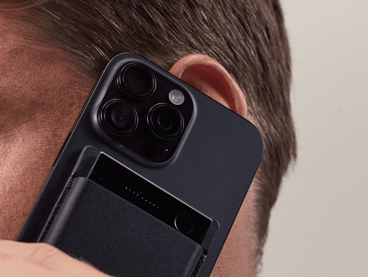 Black Plaud Note attached to a smartphone, recording a call while held to a person's ear.