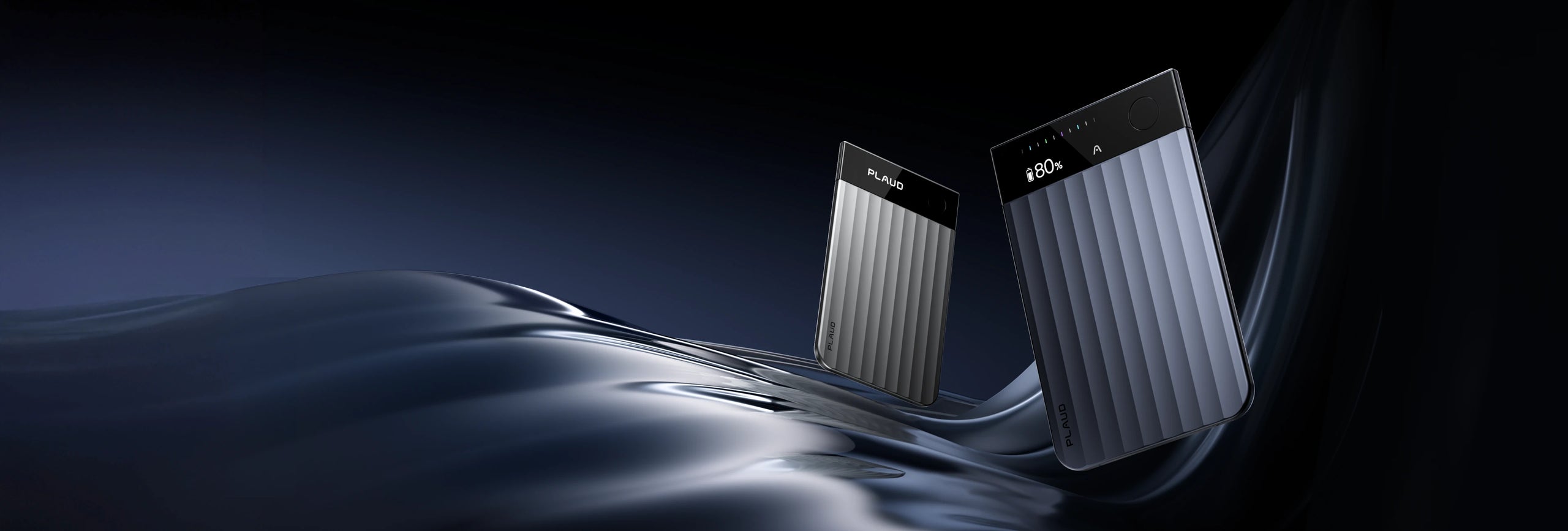 Silver and navy blue Plaud Note Pro recorders with ribbed bodies and display screens on a dark, abstract background.