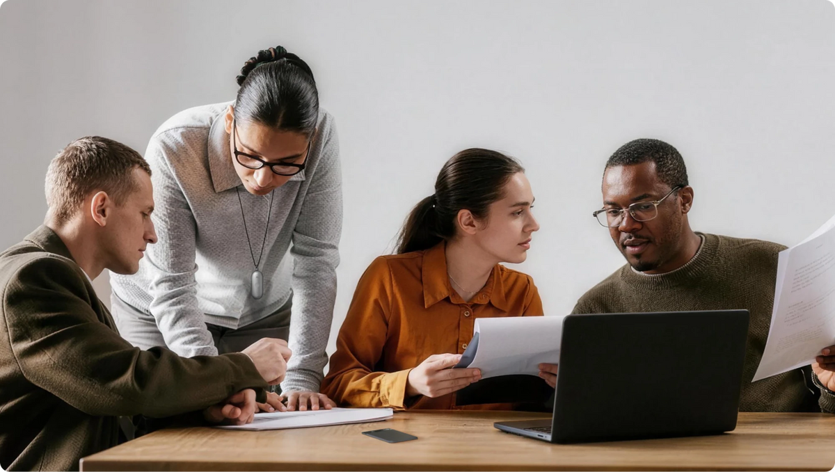 Professionals collaborating at a table; woman wears a silver Plaud NotePin on a lanyard.