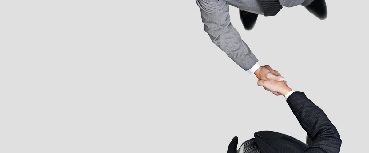 Top-down view of two business professionals in suits shaking hands against a light gray background.