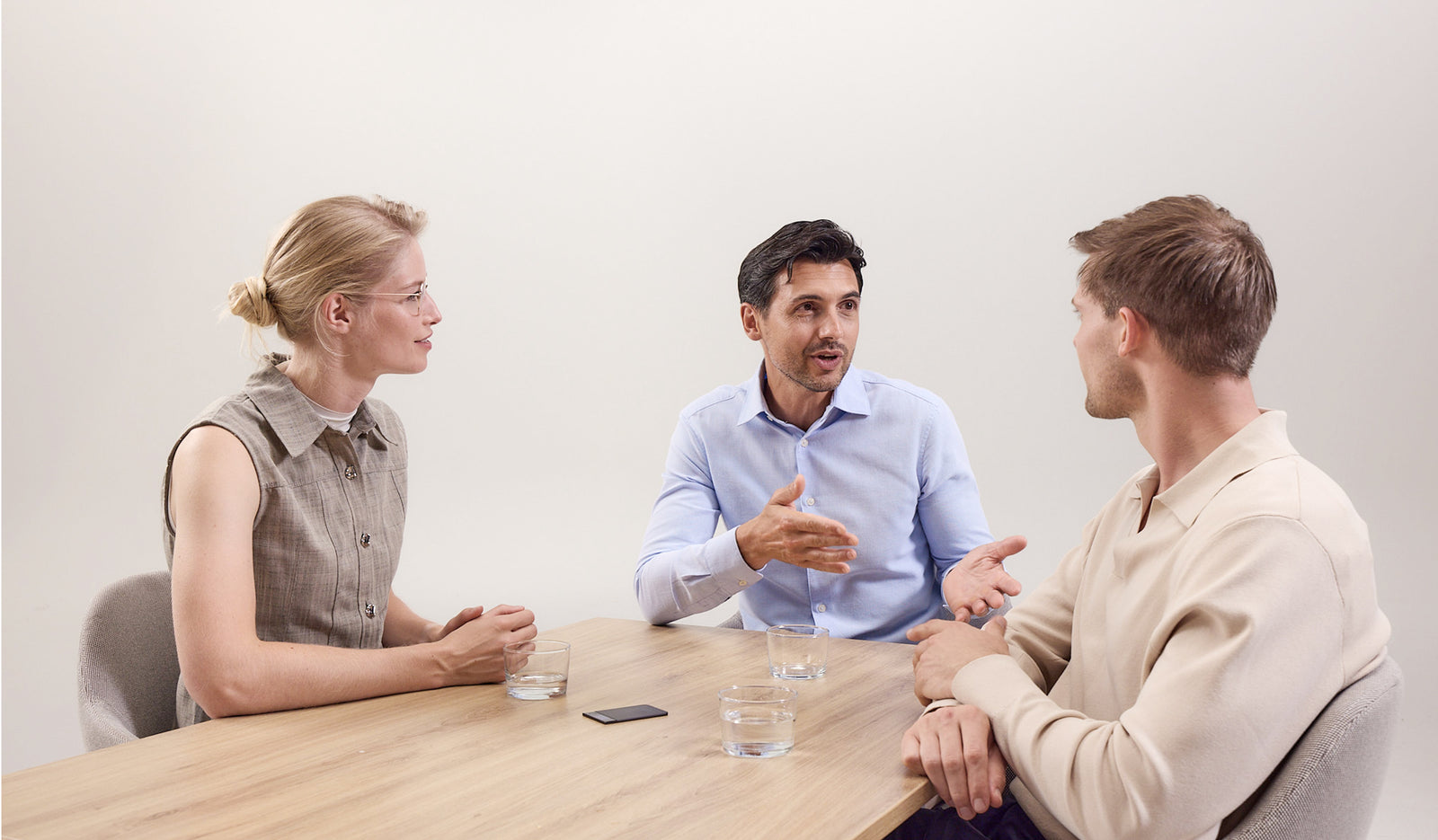 Three people talk at a table with a black Plaud Note recording the discussion.