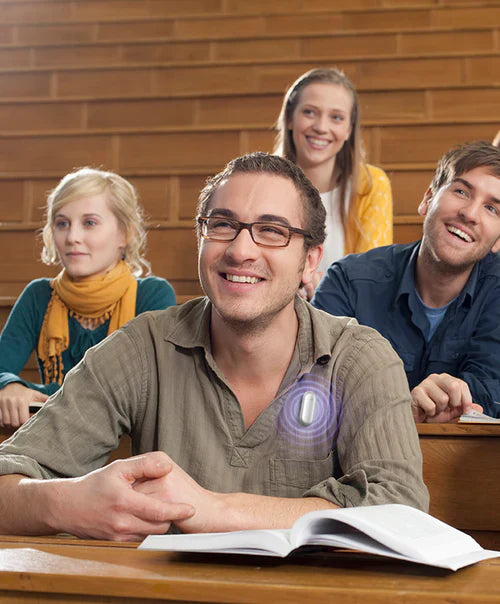 A man wearing a silver Plaud NotePin on his shirt while attending a lecture in a classroom.