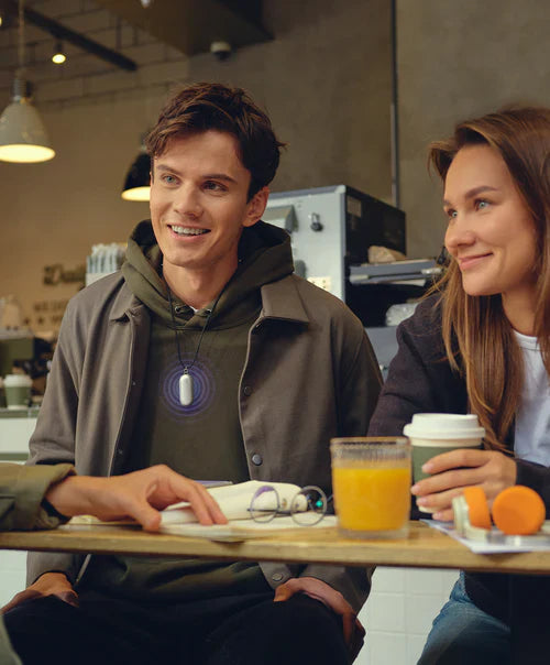 Man wearing a silver Plaud NotePin on a lanyard during a conversation in a cafe.